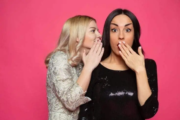 A young blonde woman sharing gossip with another another woman.