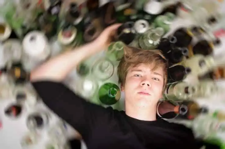 Young boy surrounded by empty bottles of alcohal.