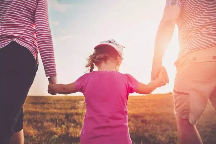 Parents holding their daughter's hands and walking in the field