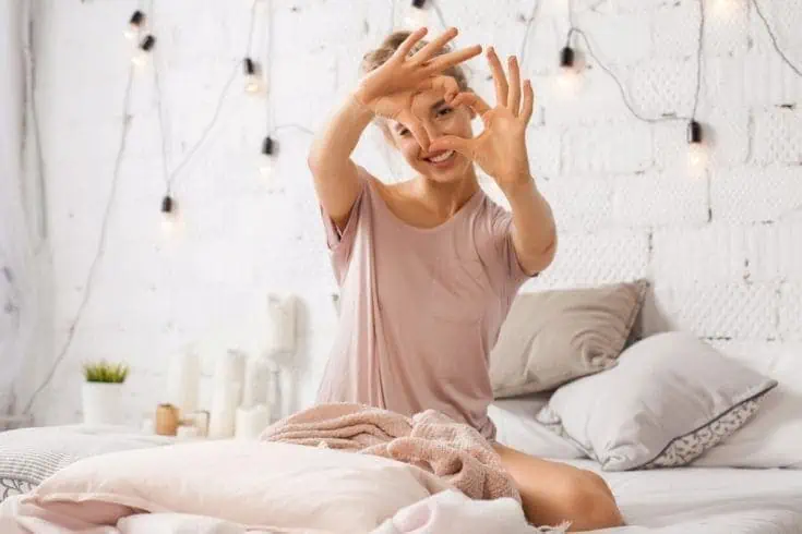 A young woman sitting on the bed and making a heart with her hands