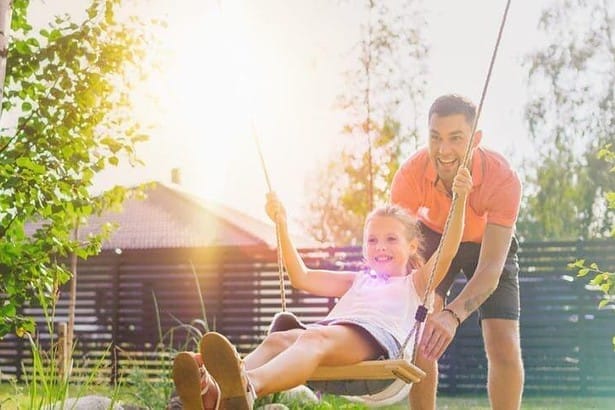 Father pushing his daughter on a swing and smiling