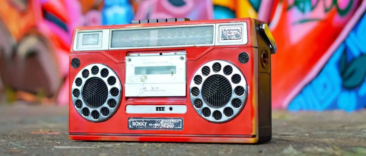 Vintage red boombox on street with colorful graffiti wall behind it.