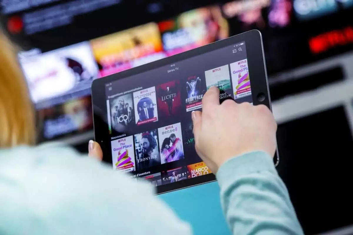 Benon, France - January 21, 2018: Woman Holding a touch pad and switching channels on France Netflix HomePage. with TV set on background. Netflix Inc. is an American multinational entertainment company founded on 1997.