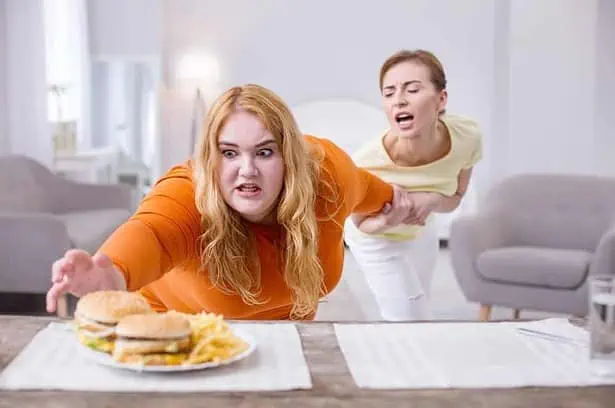 Stop. Excited stout woman reaching for a sandwich and her friend holding her.