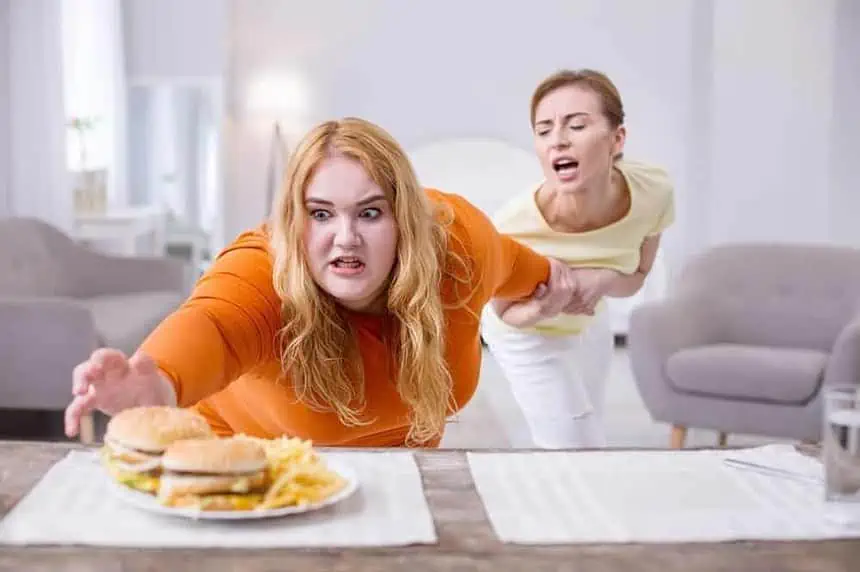 Stop. Excited stout woman reaching for a sandwich and her friend holding her.