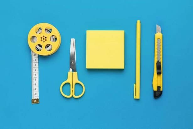 Yellow pen, measuring tape, knife and scissors on a blue background. The concept of creativity and education. Flat lay.