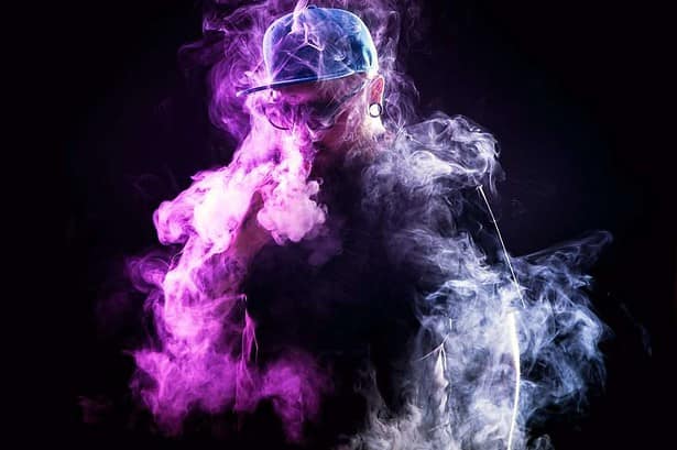 Men with beard in sunglasses vaping and releases a cloud of vapor.