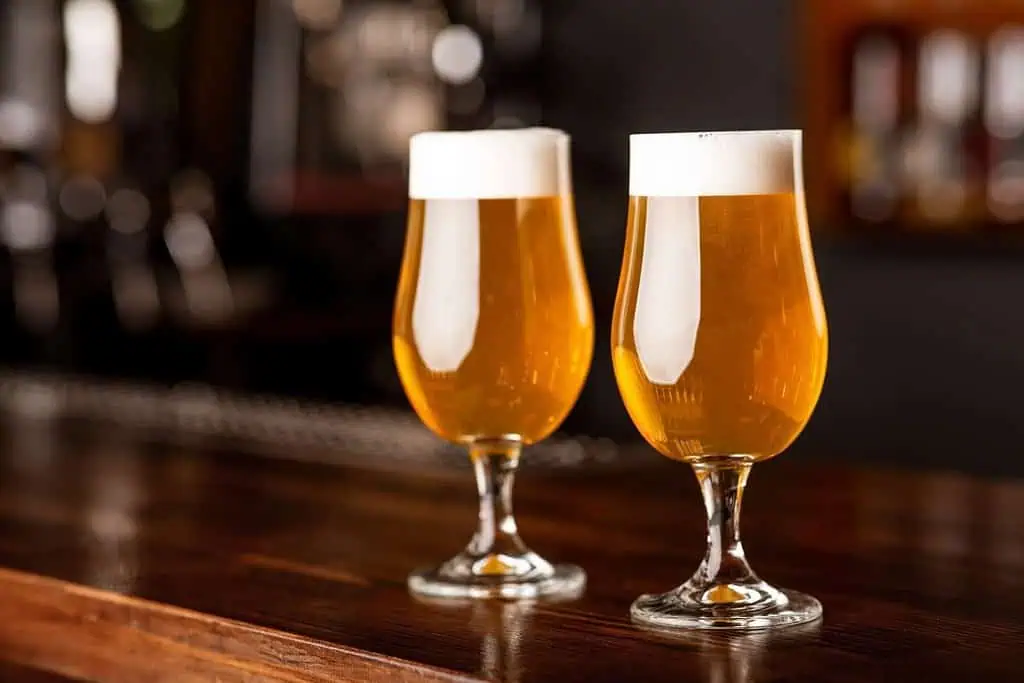 Light beer for clients. Two wine glasses on wooden bar counter in blurred interior of pub, close up. 