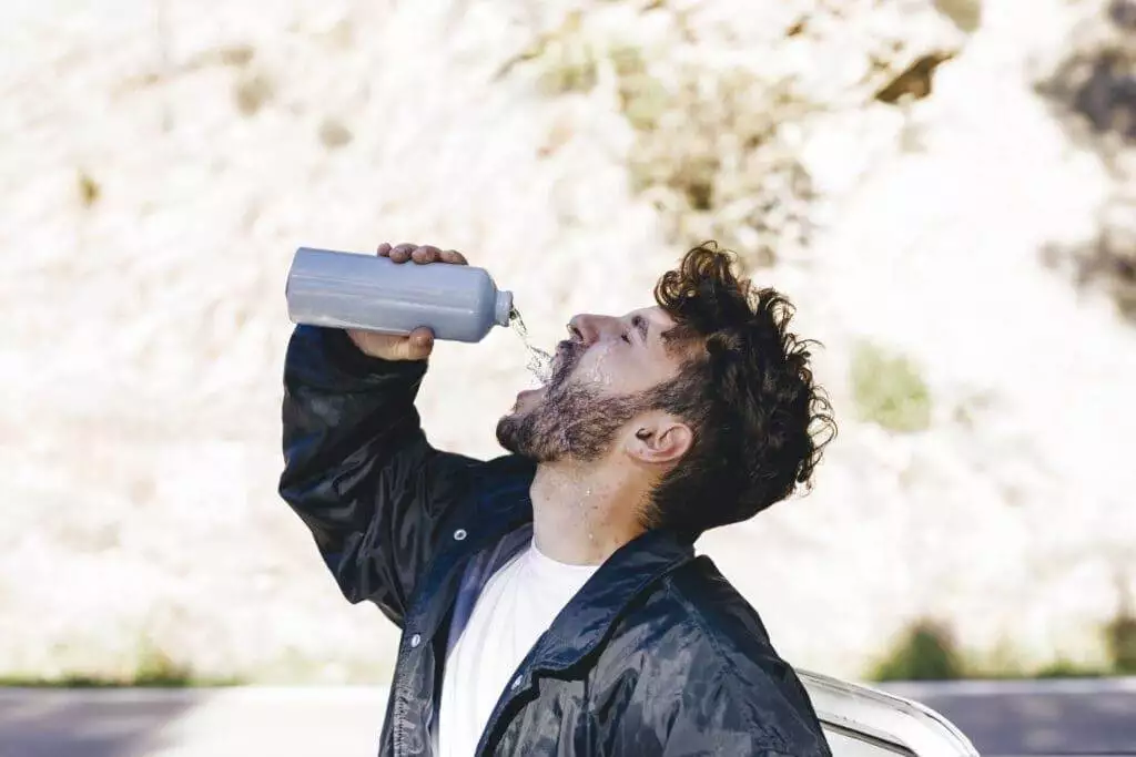 Man drinking from bottle, staying hydrated outdoors.