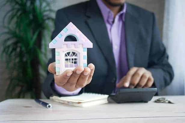 Man calculating finances and holding house model.