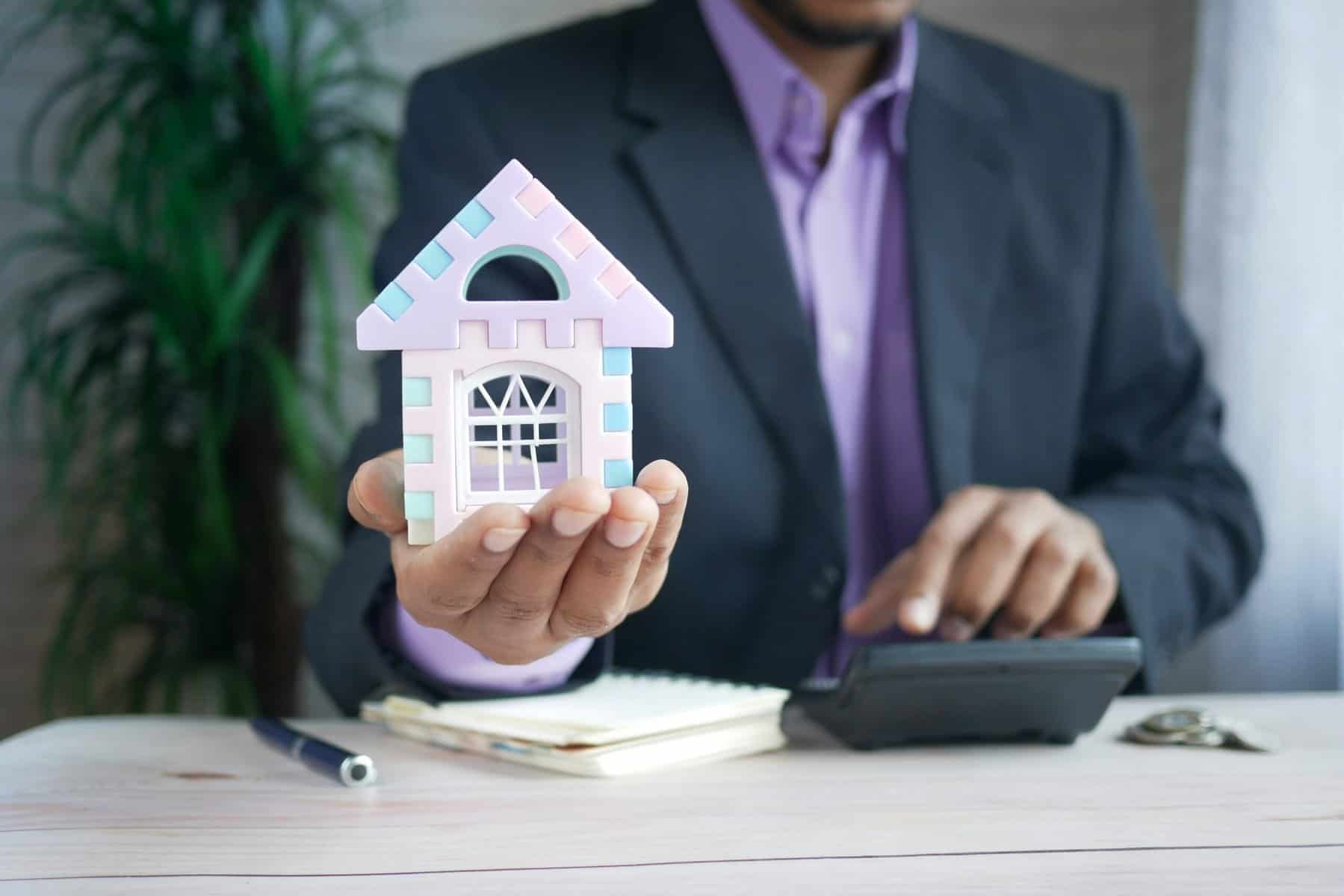 Man calculating finances and holding house model.