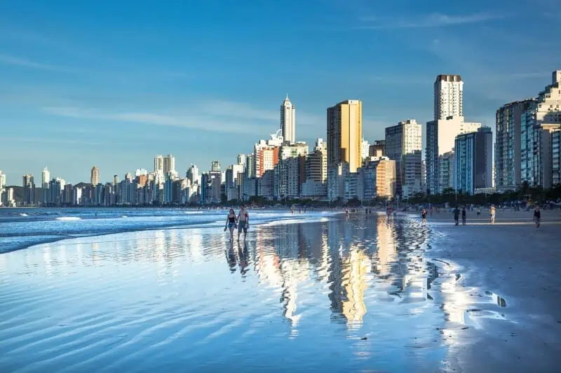 Miami city skyline with tall buildings reflected on the wet sandy beach.