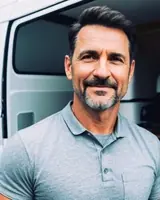 Confident man standing outdoors with a truck in the background.