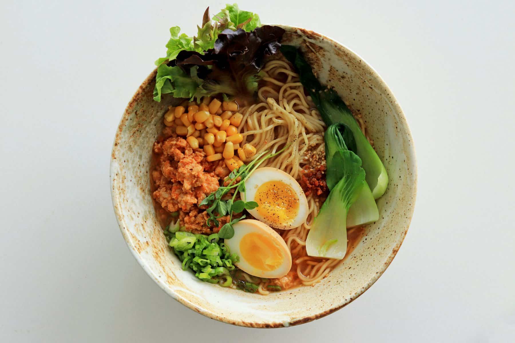 Delicious ramen bowl featuring noodles, boiled eggs, fresh greens, corn, and vegetables in a savory.