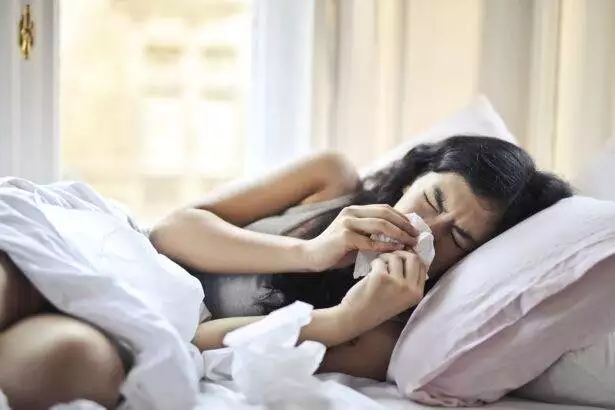 Sick woman blowing her nose in bed