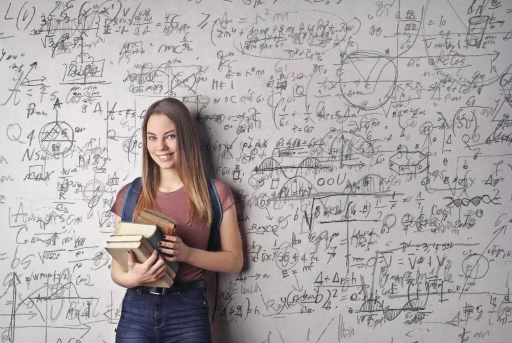 Equations in Disguise: How To Know If An Equation Is A Function 4 A girl holding a few books is standing in front of a white wall with equations scribed on it.