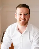 A professional man smiling confidently in a business setting, dressed in a white shirt.