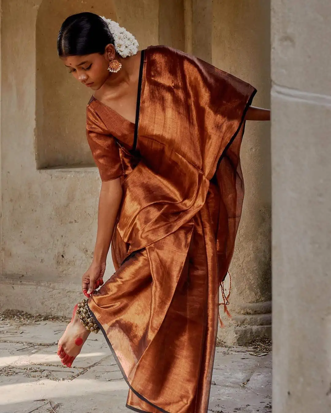Woman in traditional brown saree with ethnic jewelry.