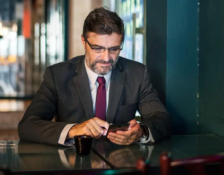 Businessman in a suit using a smartphone at a cafe table, focused on his device.