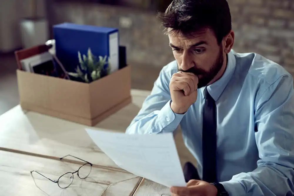 Businessman with box of belongings reviewing documents.