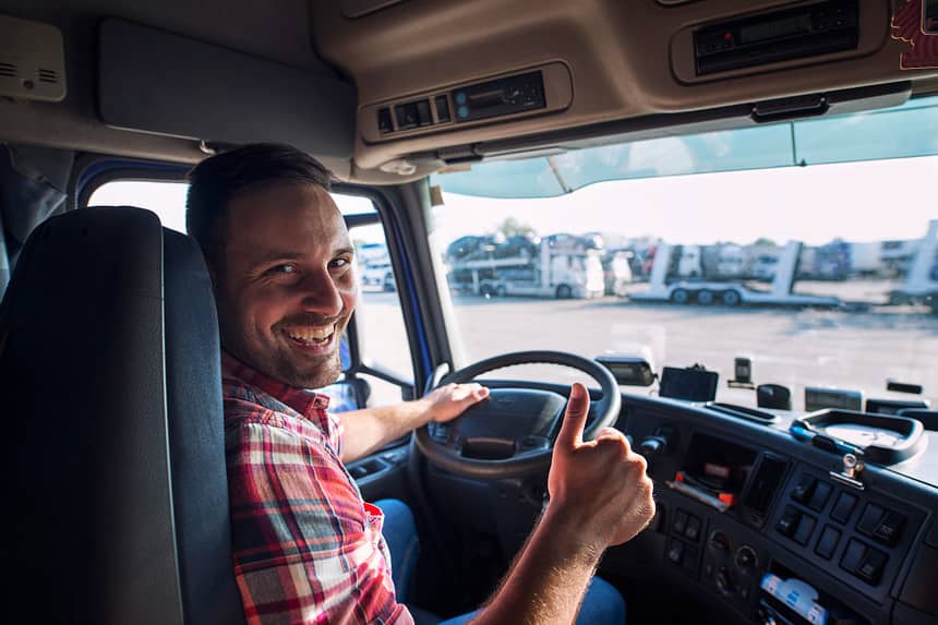 Smiling truck driver giving a thumbs-up inside his cab.