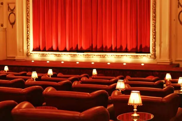 Theatre seating with plush chairs, small lamps, and a red curtain stage, creating an elegant and coz.