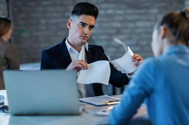 Manager critically reviewing reports with employee in office setting