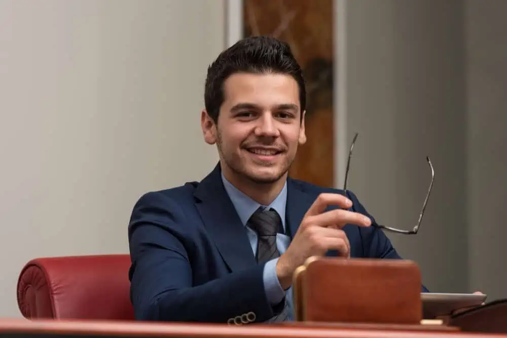 Businessman smiling in a formal office environment holding glasses.