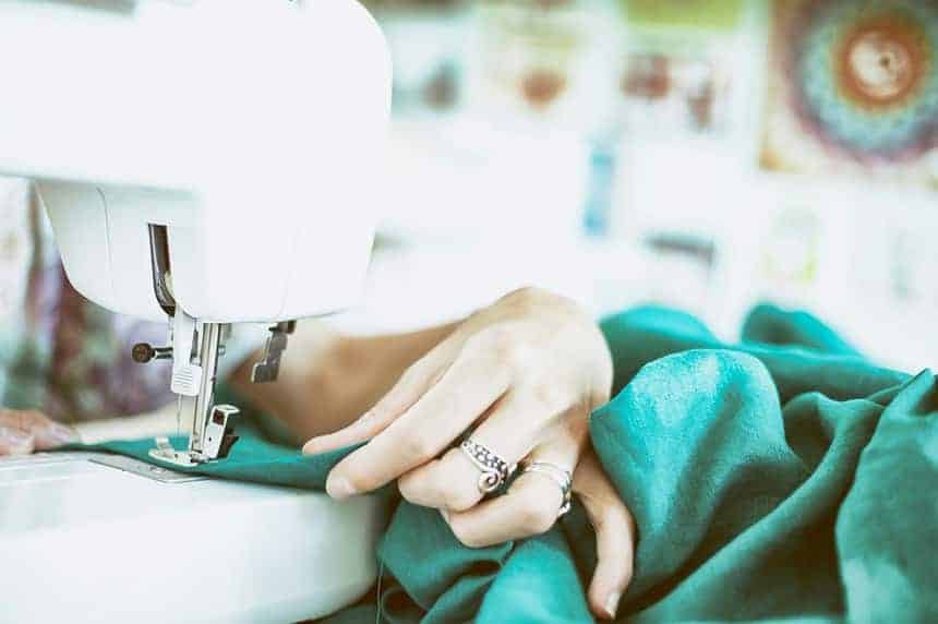 Close-up of hands sewing green fabric on a sewing machine.