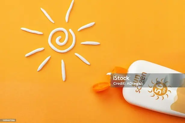 Sunscreen bottle with cream sun shape on orange background.