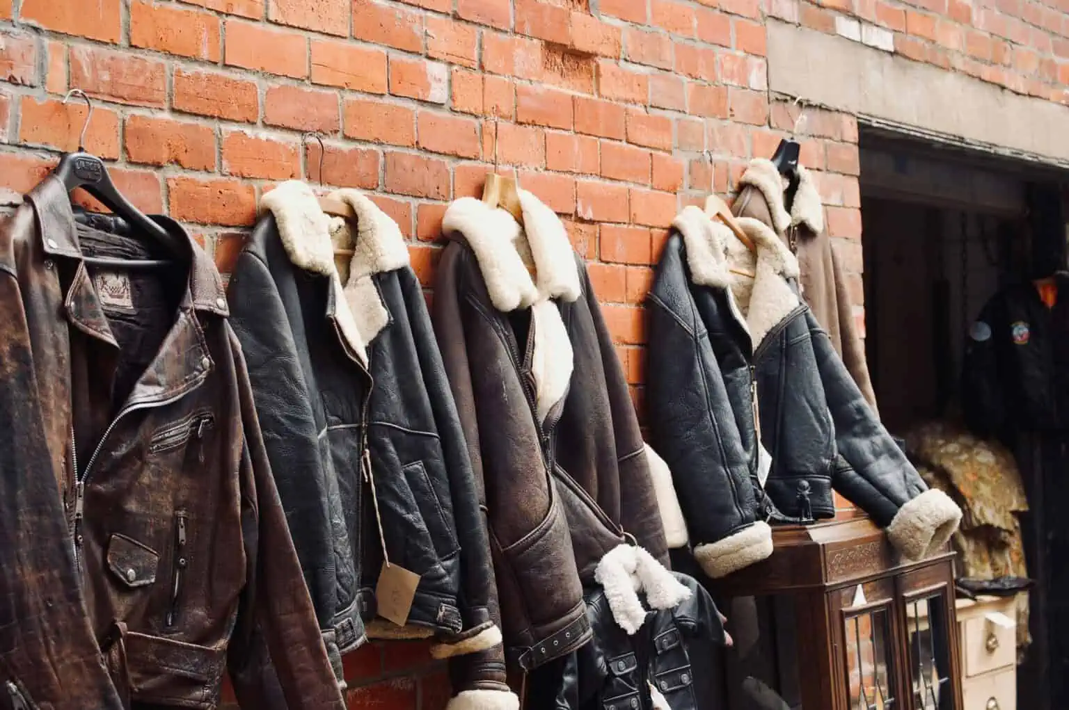 Vintage leather jackets on sale beside a brick wall.