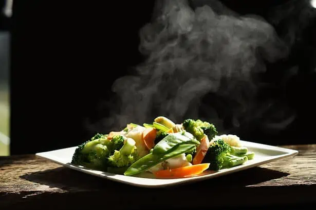 Healthy steamed vegetables with steam rising, on a rustic wooden surface.