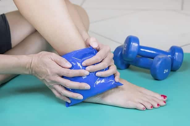 Woman applying ice pack to injured ankle after workout
