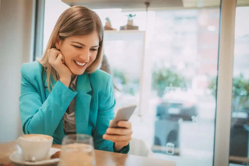 15 Ways to Keep Yourself Entertained on Your Mobile Phone When You're Bored 3 Beautiful young smiling woman using smart phone in a cafe.