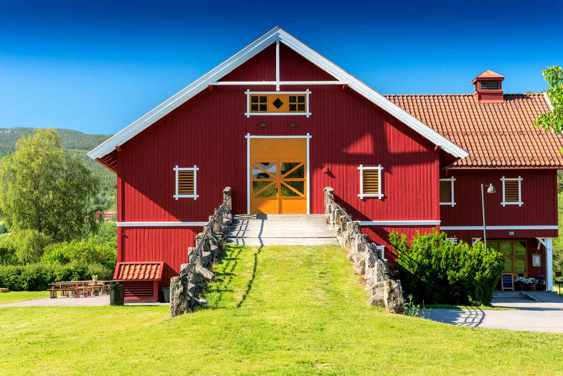 Red barn with staircase, lush green landscape, and bright blue sky, ideal for rural or farm-themed c.