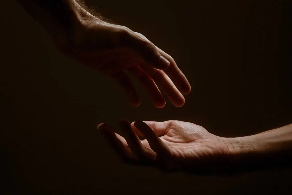 Helping hands reaching out in a dark setting, symbolizing support and connection.