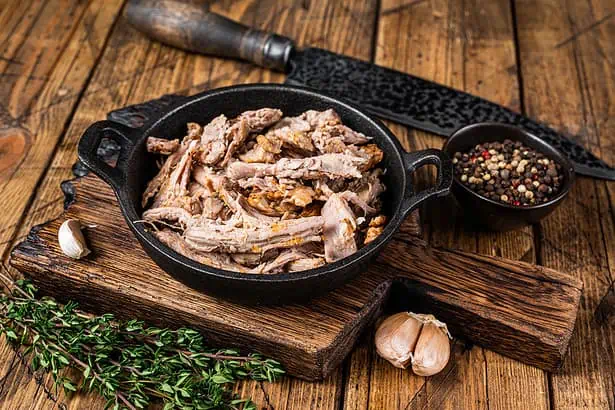 Delicious pulled pork served in a rustic cast iron skillet with herbs and spices. Perfect for hearty.