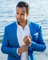 Confident man in blue blazer standing by the water, looking thoughtful.