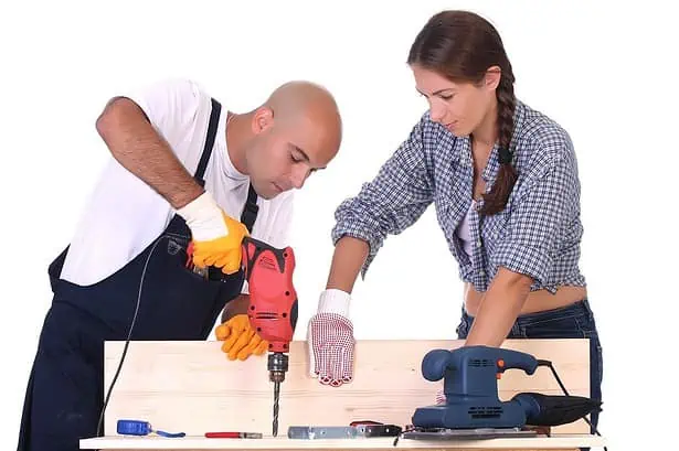 Man and woman working together on a woodworking project with power tools.