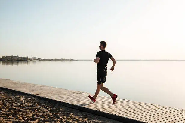 A man jogging along a wooden pathway by the calm water during sunset.