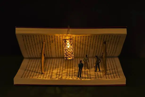 Open book with tiny figurines and a glowing lantern inside, creating a captivating miniature scene.
