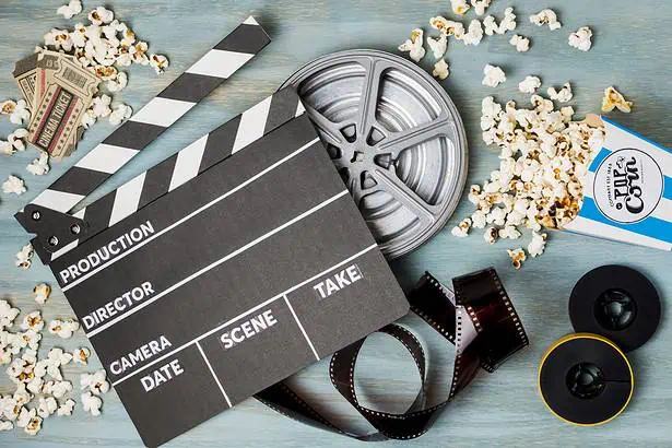 Film production clapperboard with reel, popcorn, and camera for movie making.