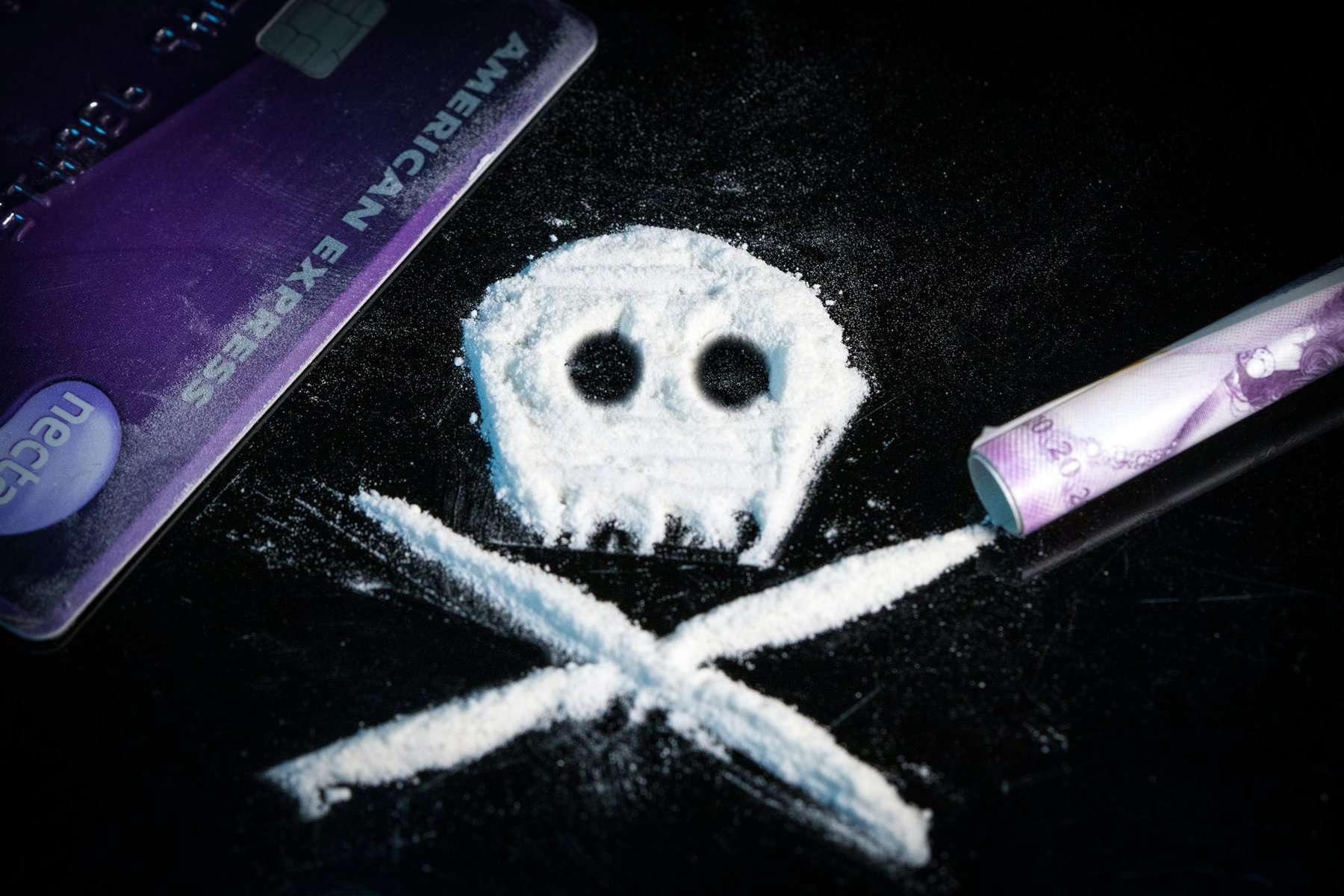 Cocaine powder shaped like a skull and crossbones on black surface.