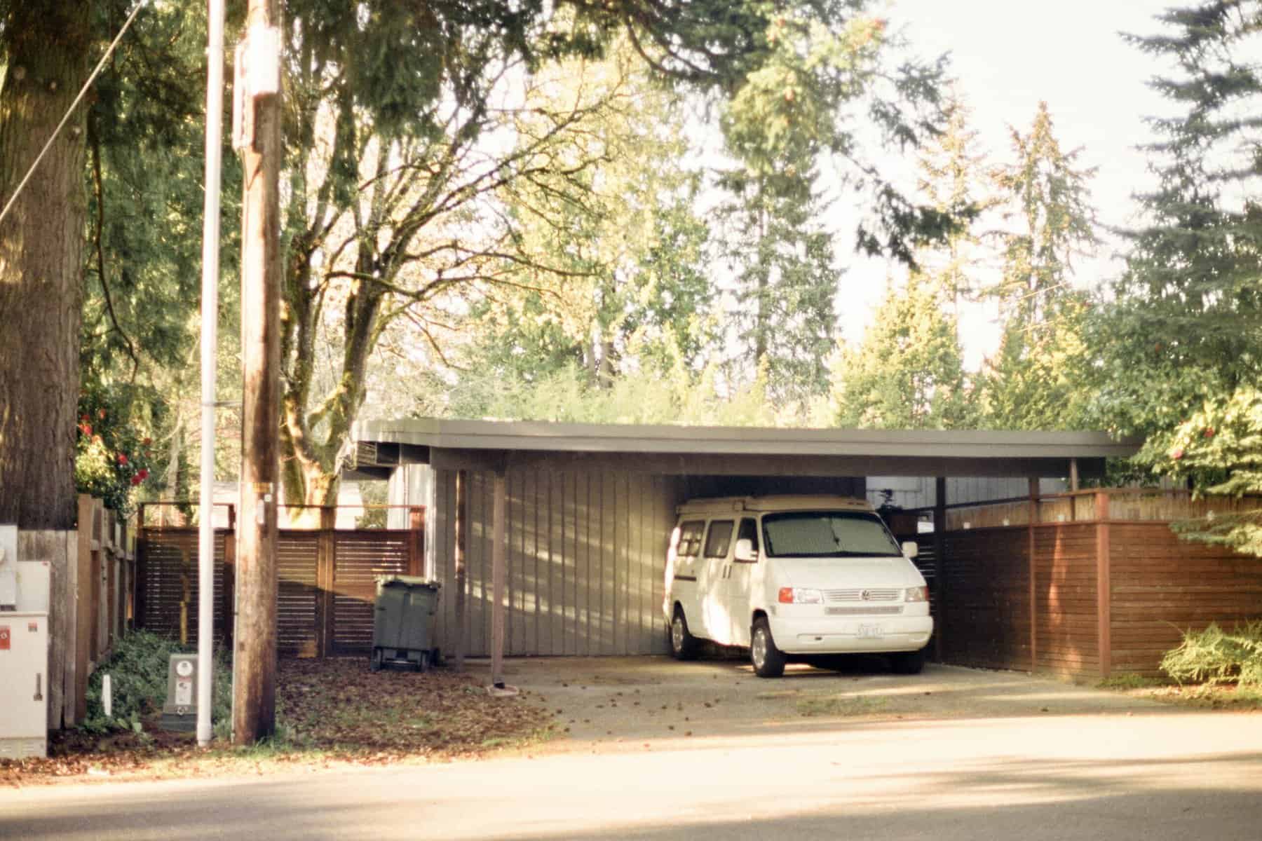 Garage with white van parked inside, surrounded by trees and wooden fencing.