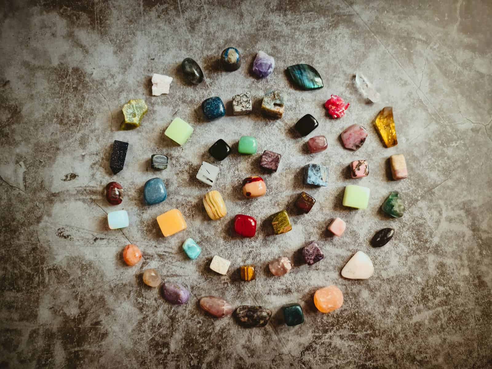 Jewelry gemstones arranged in a spiral pattern on a textured surface.