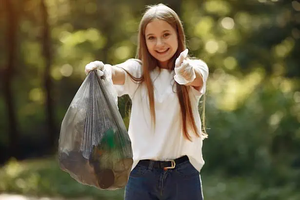 Young girl holding a trash bag outdoors, promoting environmental cleanup.