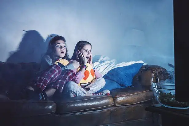 Two girls watching TV on a sofa during a cozy night in.