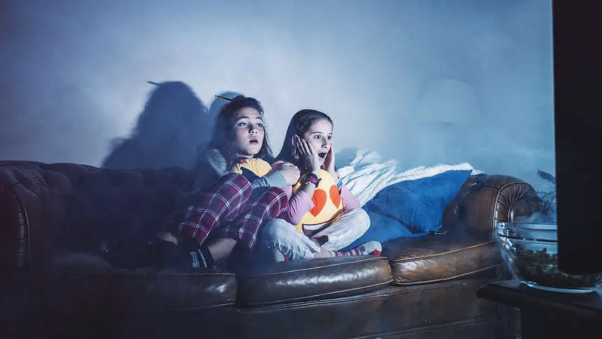 Two girls watching TV on a sofa during a cozy night in.