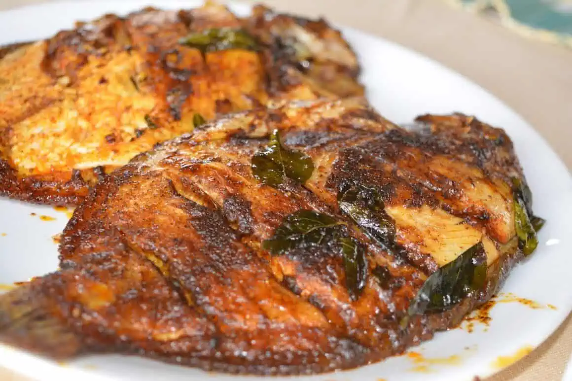 Delicious grilled fish seasoned with spices and herbs, served on a white plate.