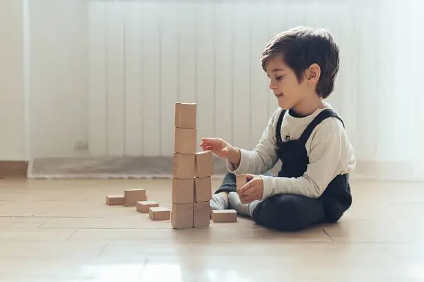 Young boy stacking wooden blocks on the floor indoors.